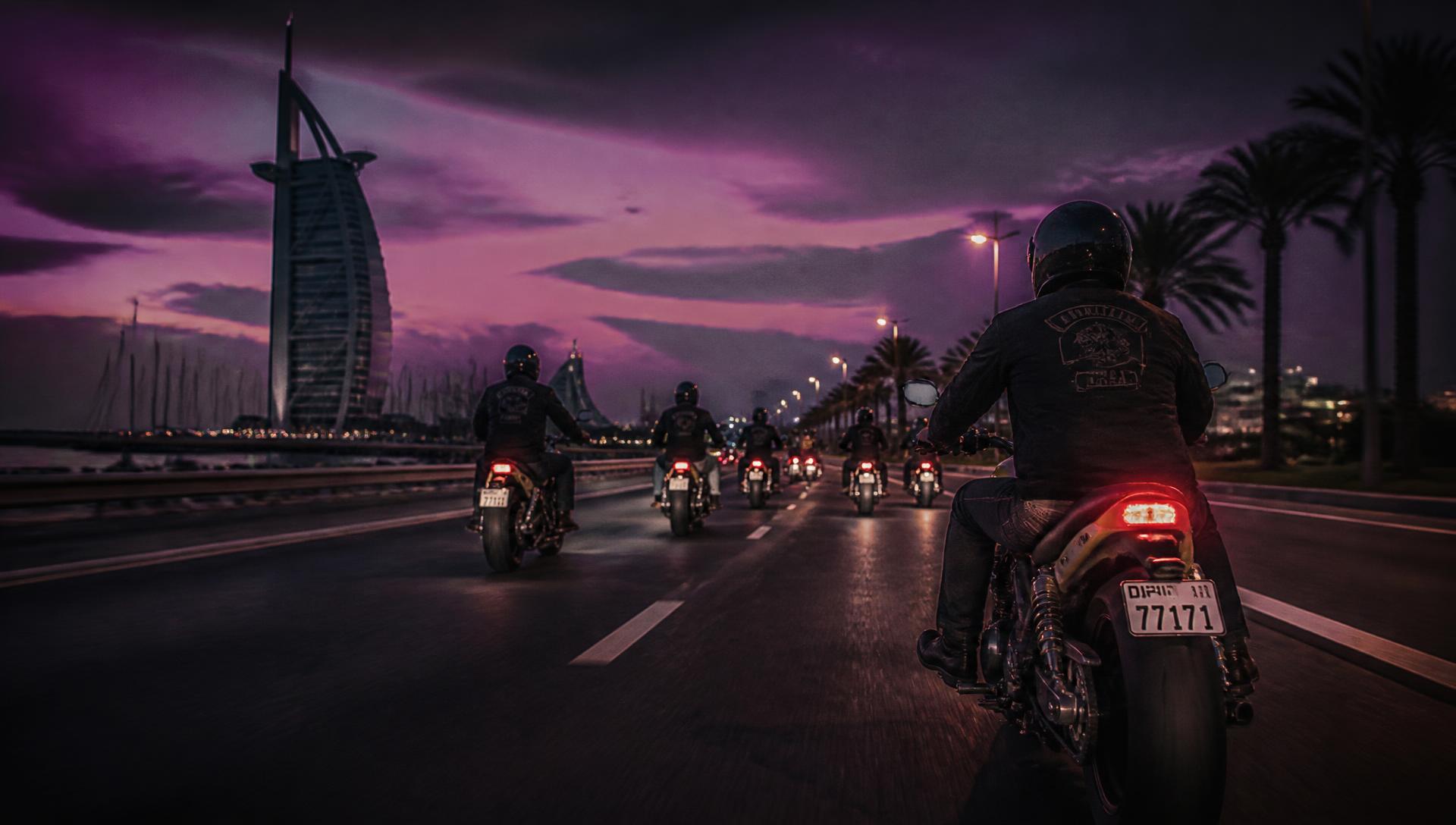 Group of motorcyclists riding a coastal Dubai highway at dusk